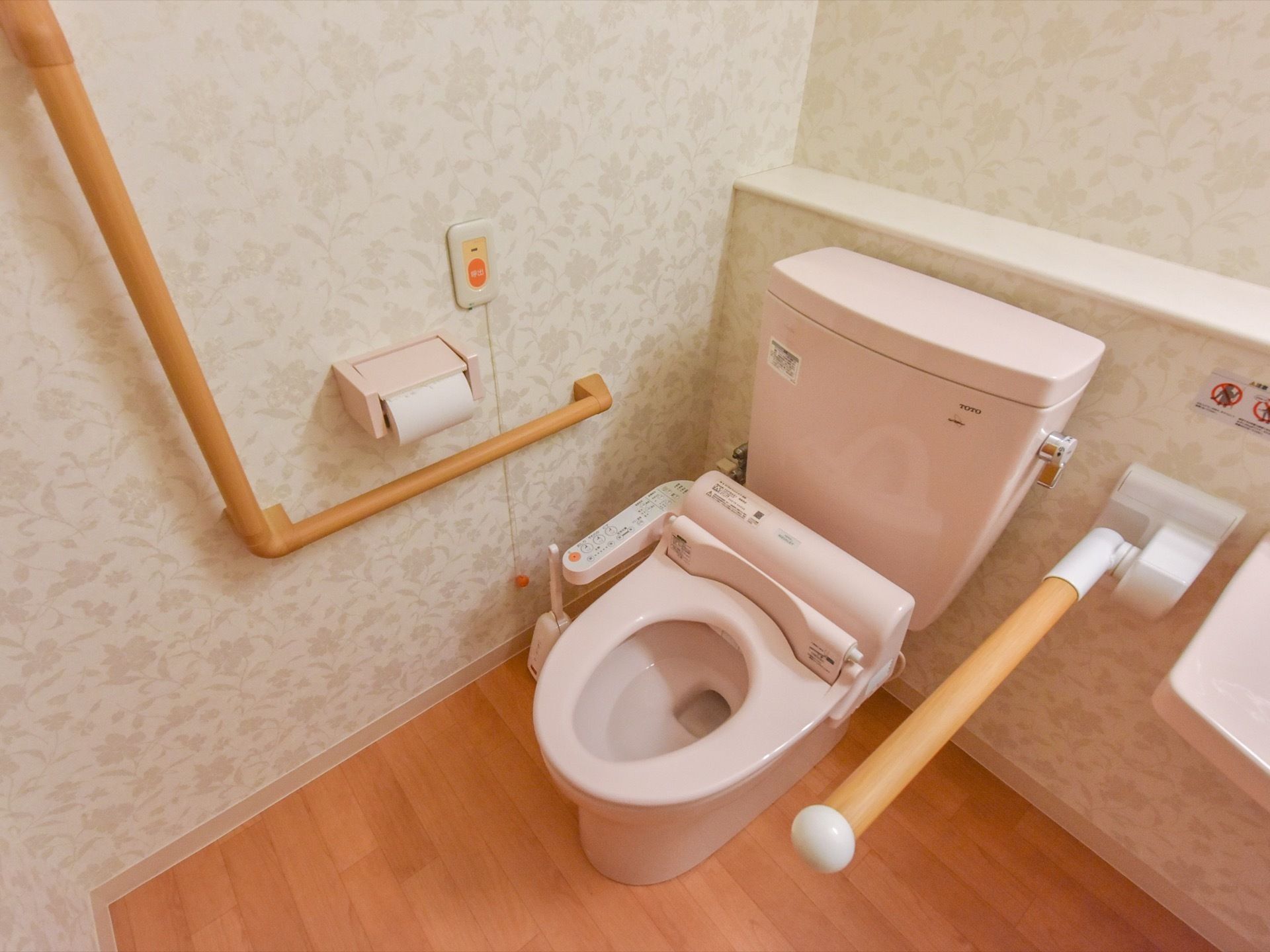 トイレは洗浄機能付きの洋式である。便器の両側に手すりが取り付けられている。緊急用のブザーもある。壁紙は花柄である。