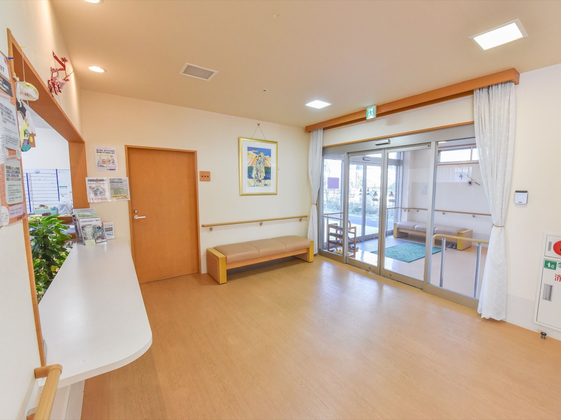 玄関ホールの壁際や風除室の中にはソファーが設置されている。手すりも取り付けられている。受付カウンターの内部には、観葉植物がある。