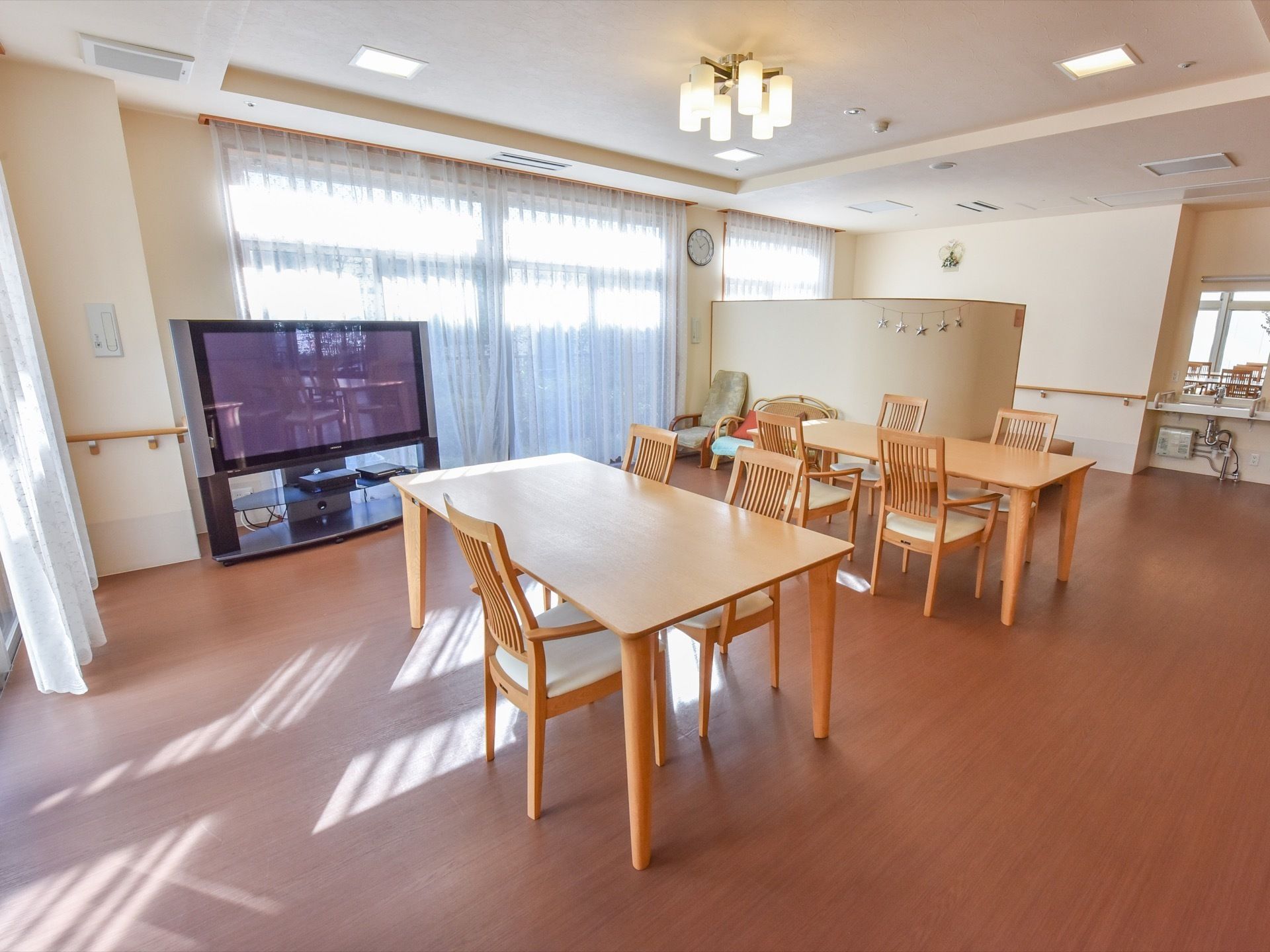 食堂には、窓から日差しが差し込み、明るい。テーブルやイスはナチュラル系の色である。大型テレビが置かれている。