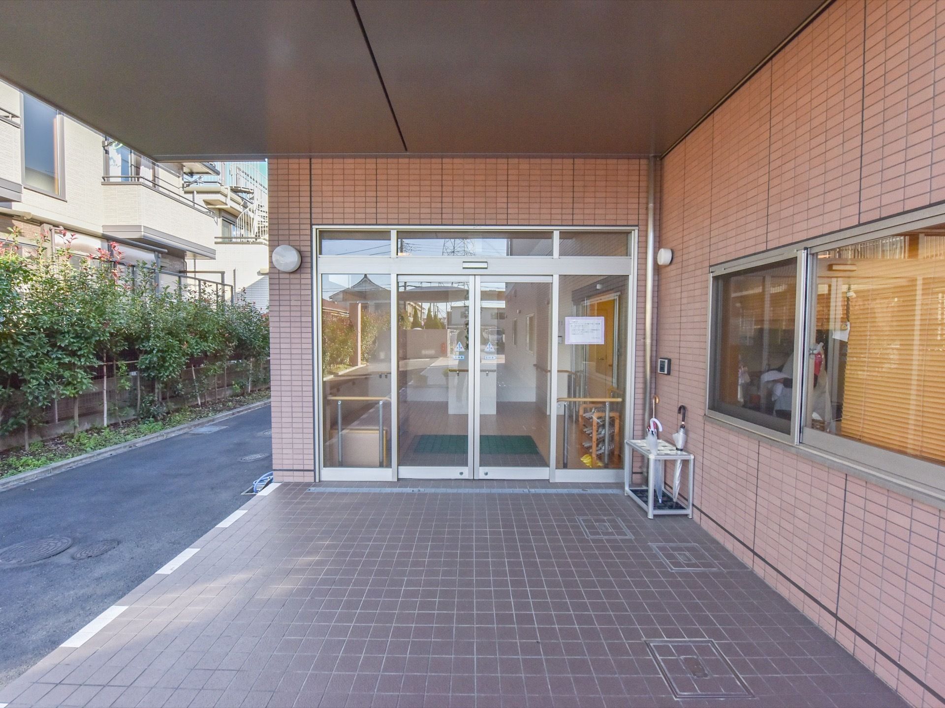 玄関の自動ドアの前には屋根が備わった広いスペースが設けられている。自動ドアからは施設内の様子がうかがえる。