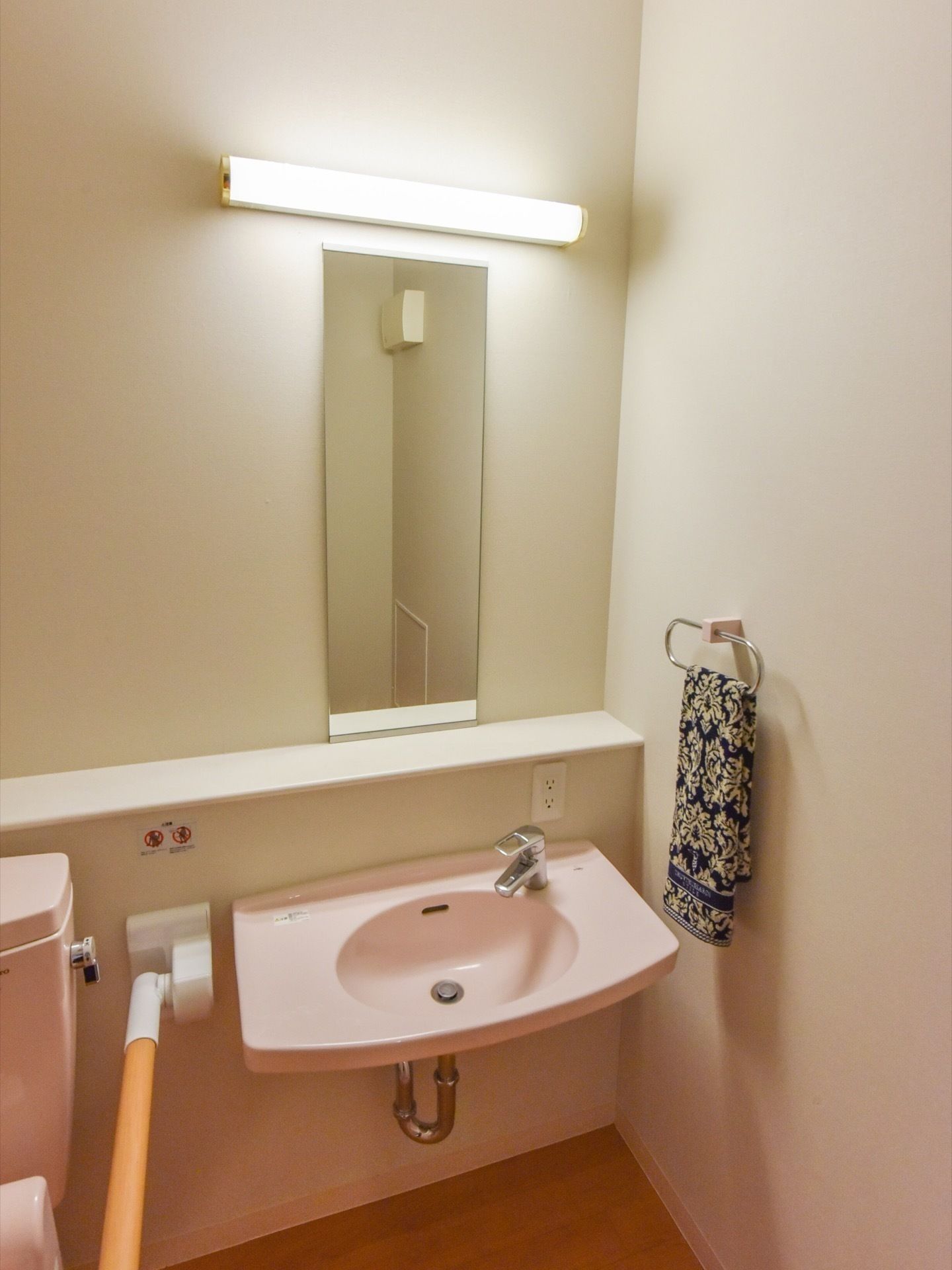 トイレの隣には洗面台がある。右側の壁にはタオル掛けがあり、鏡の前には小物をおけるようなスペースがある。