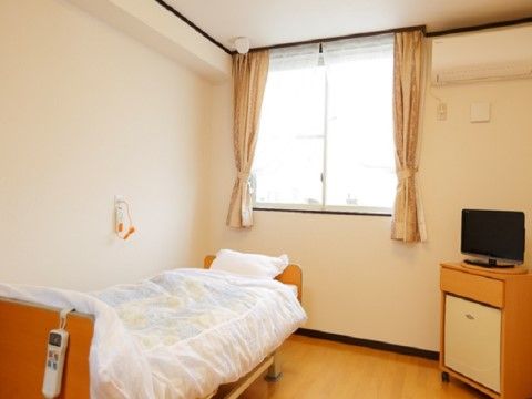 呼び出しボタン付きのベッドとテレビが置かれたワンルーム