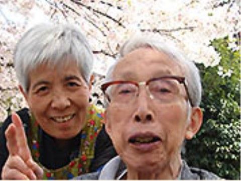桜が満開の季節に、外出先でピースサインをする笑顔の入居者様
