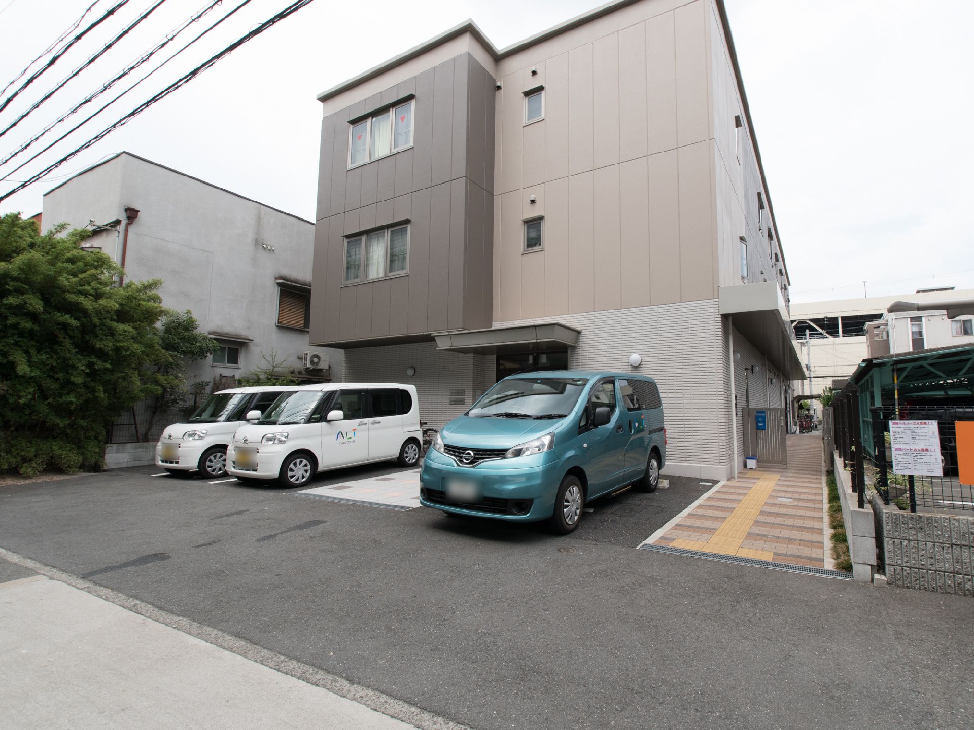 施設感がない「住宅」をイメージした外観は、玄関に雨除けの屋根があるだけのシンプル設計。建物の脇には、裏側まで行ける明るい縞模様の道がある。