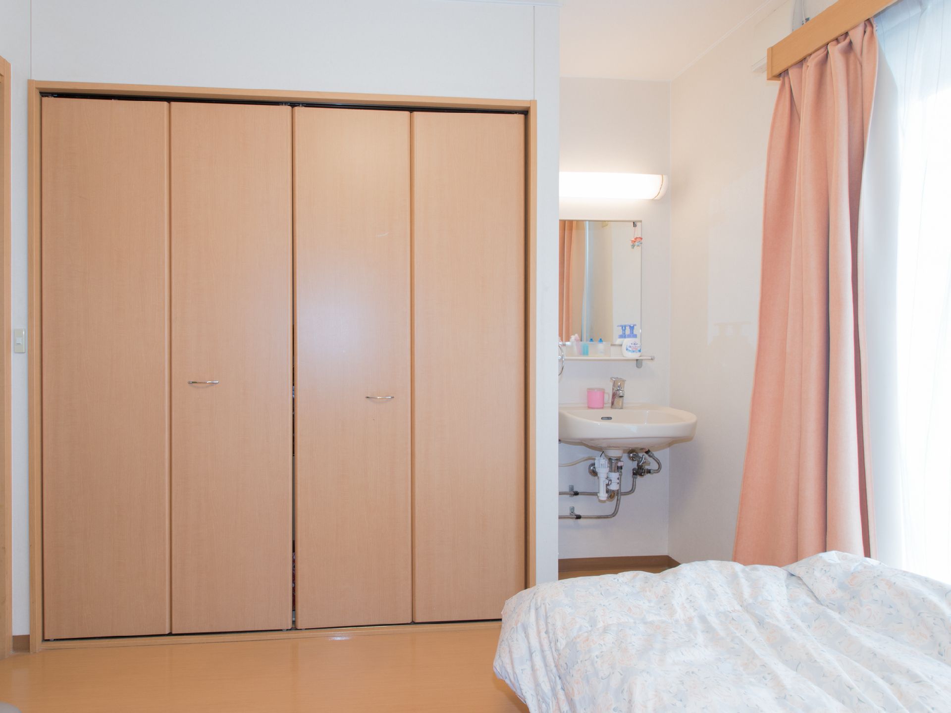 白色と茶系でまとめられた内装。木目調の両開きの折れ戸。その隣には洗面台が設置されている。洗面台上には照明と鏡が取り付けてある。
