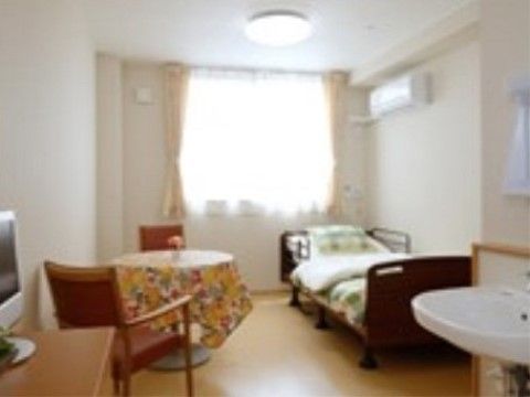 白い壁で優しいベージュ色の床には、柔らかな光が射し込んでいる。ベッドは電動で手すりもついていて、チェストやテーブルなどもある。