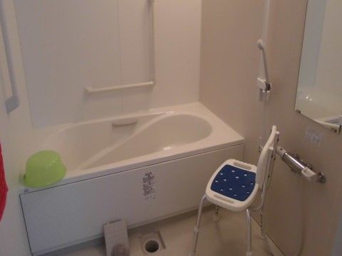 明るく掃除が行き届いた、清潔な淡いピンクの浴室である。シャワーの横や浴槽に手すりがあり、シャワー椅子も完備している。