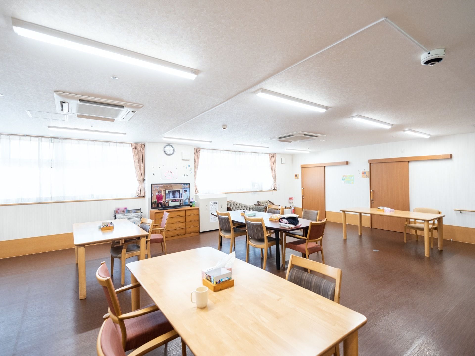 食堂の中央には、テレビが設置されている。天井に、空調機、監視カメラが取り付けてある。テーブルと椅子はスペースを取って配置されている。