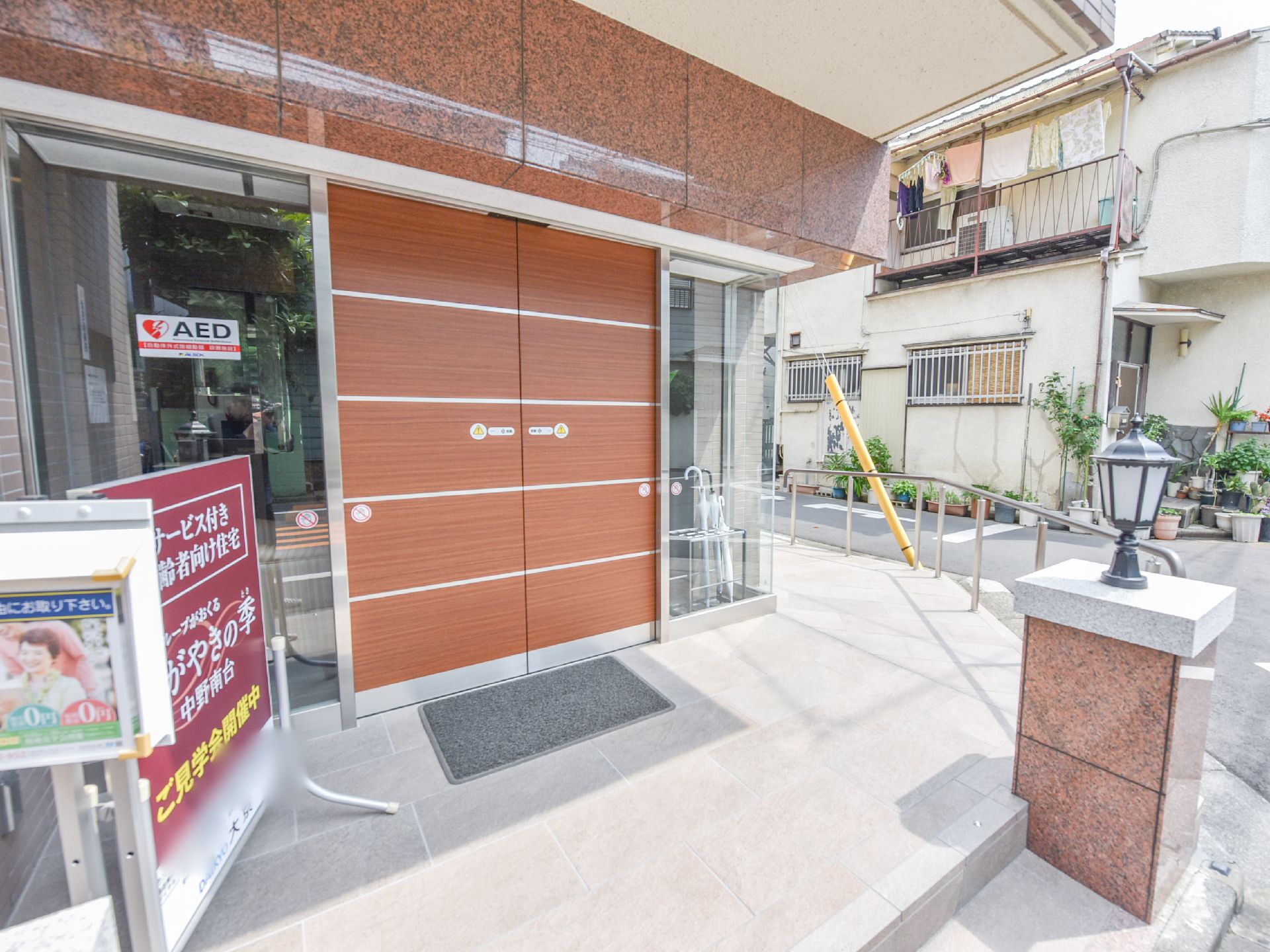 茶系の外観が落ち着いた雰囲気の施設の入り口。道路からのアプローチ低めの階段と、スロープが設置されている。