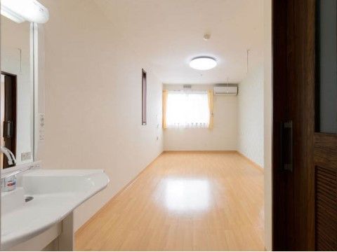 居室は広々としている。窓からは日が差し込み、照明の光と合わさって明るい部屋になっている。鏡付きの洗面台も設置されている。