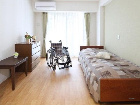 ベッド、エアコン、テーブルセットとシンプルな居室。窓からは陽が差し込んでいて、とても明るい。床はフローリングになっている。