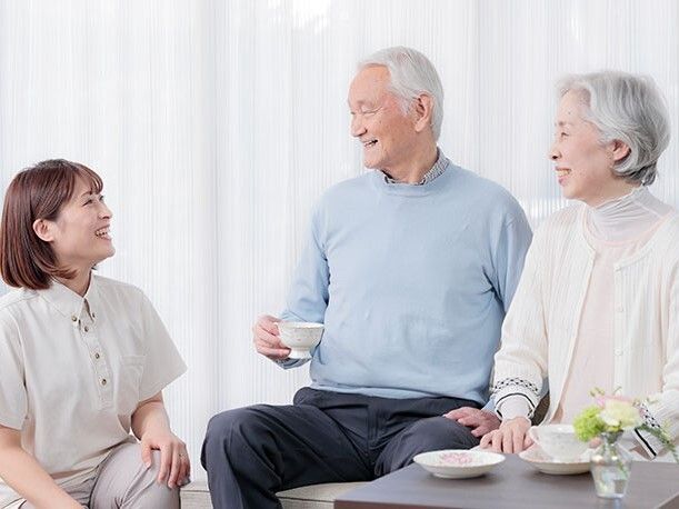 外出先でニッコリと笑う、車椅子の乗った男性とベンチに座った女性