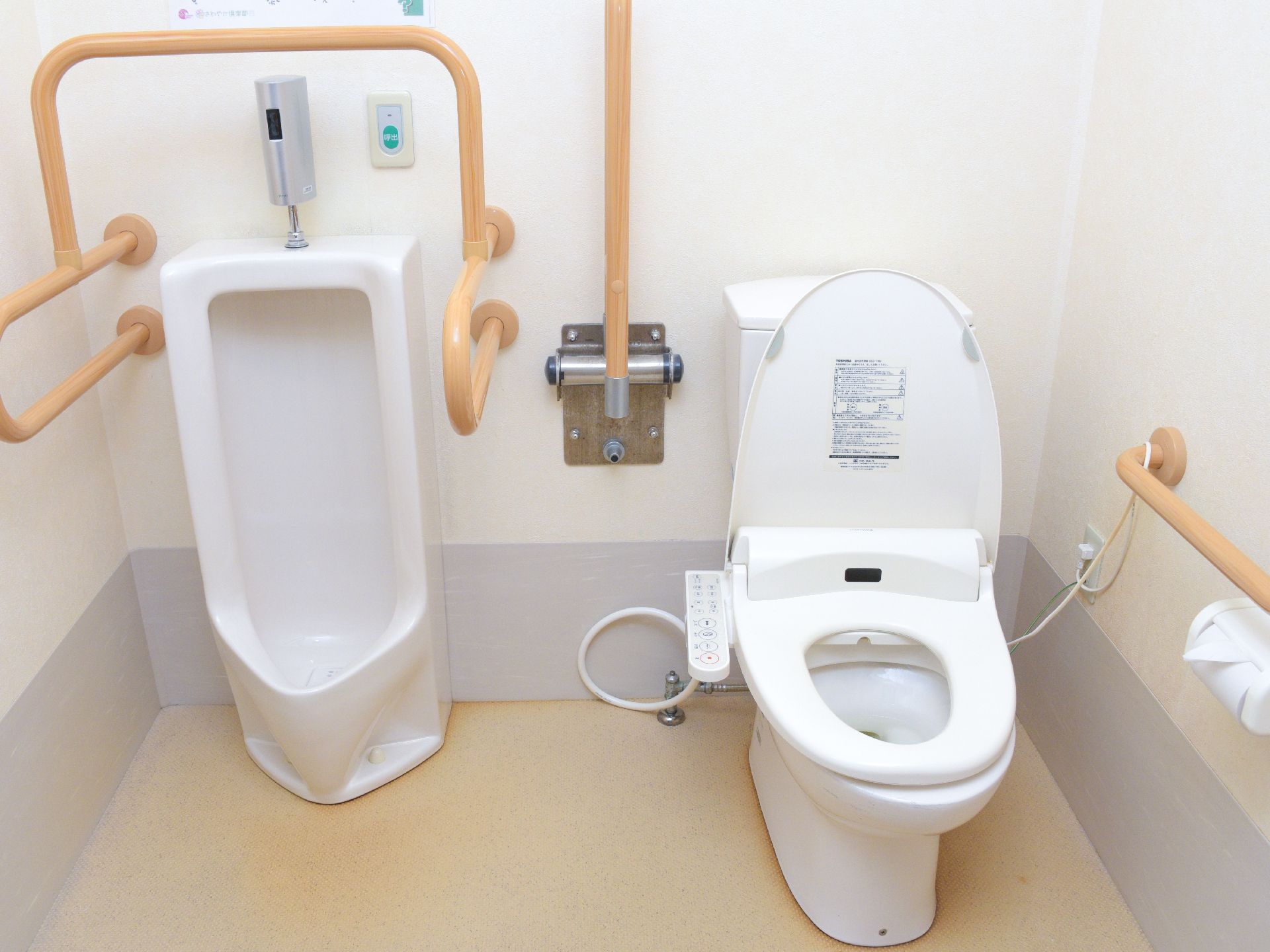 個室内に男性用トイレと洋式トイレが備わっている。手摺、緊急呼出ボタン、温水洗浄便座が設置されている。