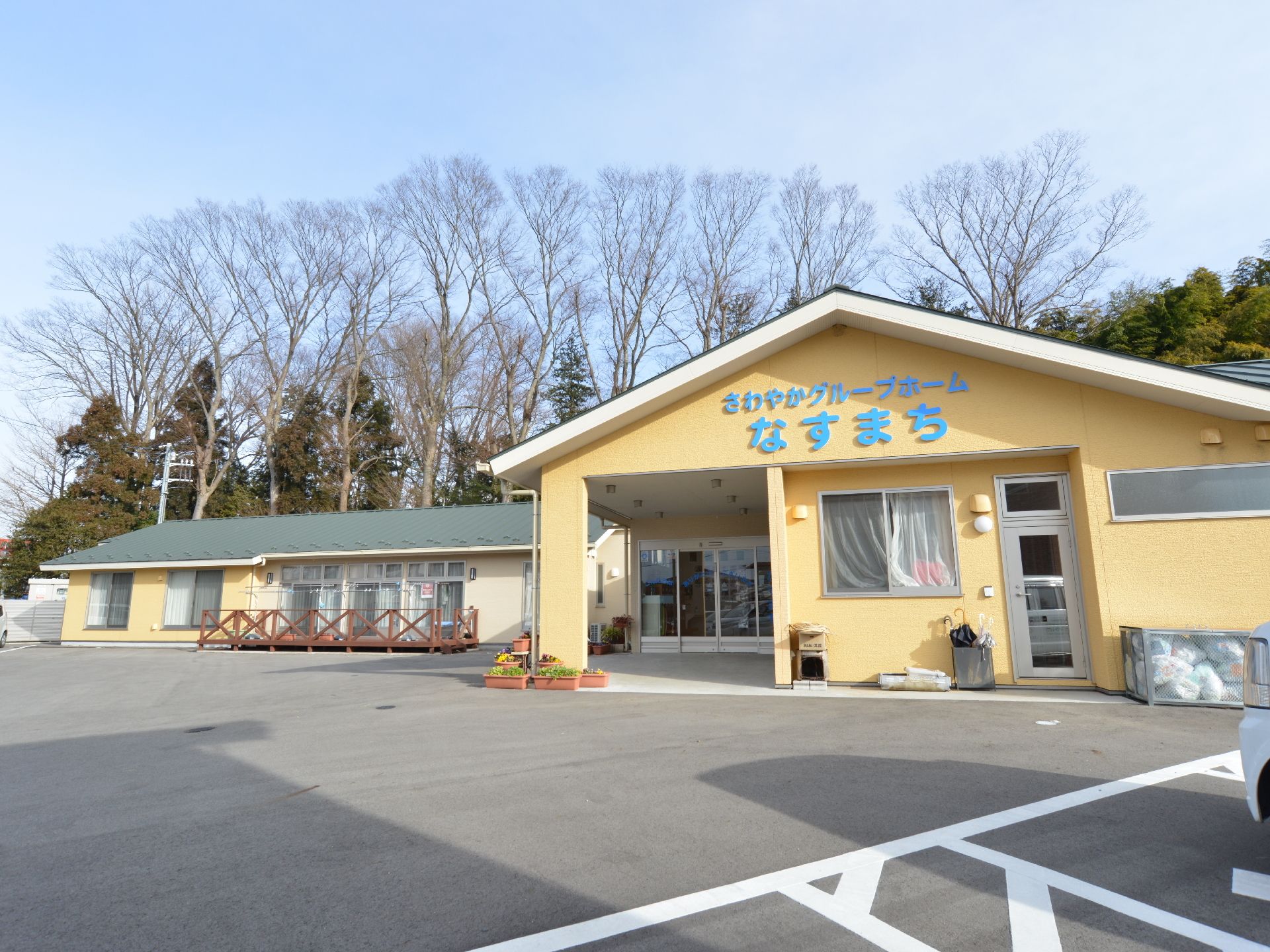 広い駐車場が併設された、黄色い一軒家型のグループホーム