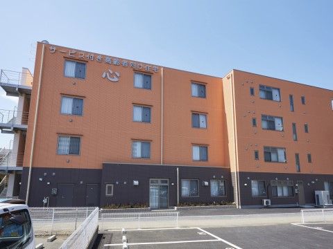 ４階建ての建物。黒とレンガ色のツートンが印象的である。広い駐車場があり、ご家族様がご来訪の際に便利である。