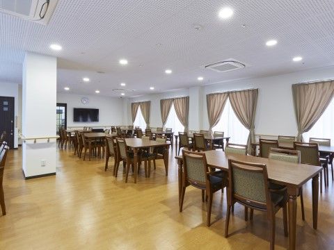 広々としたリビングには、茶色いテーブルと椅子がたくさん配置されている。また手すりも設置されているので移動の負担を減らすことができる。
