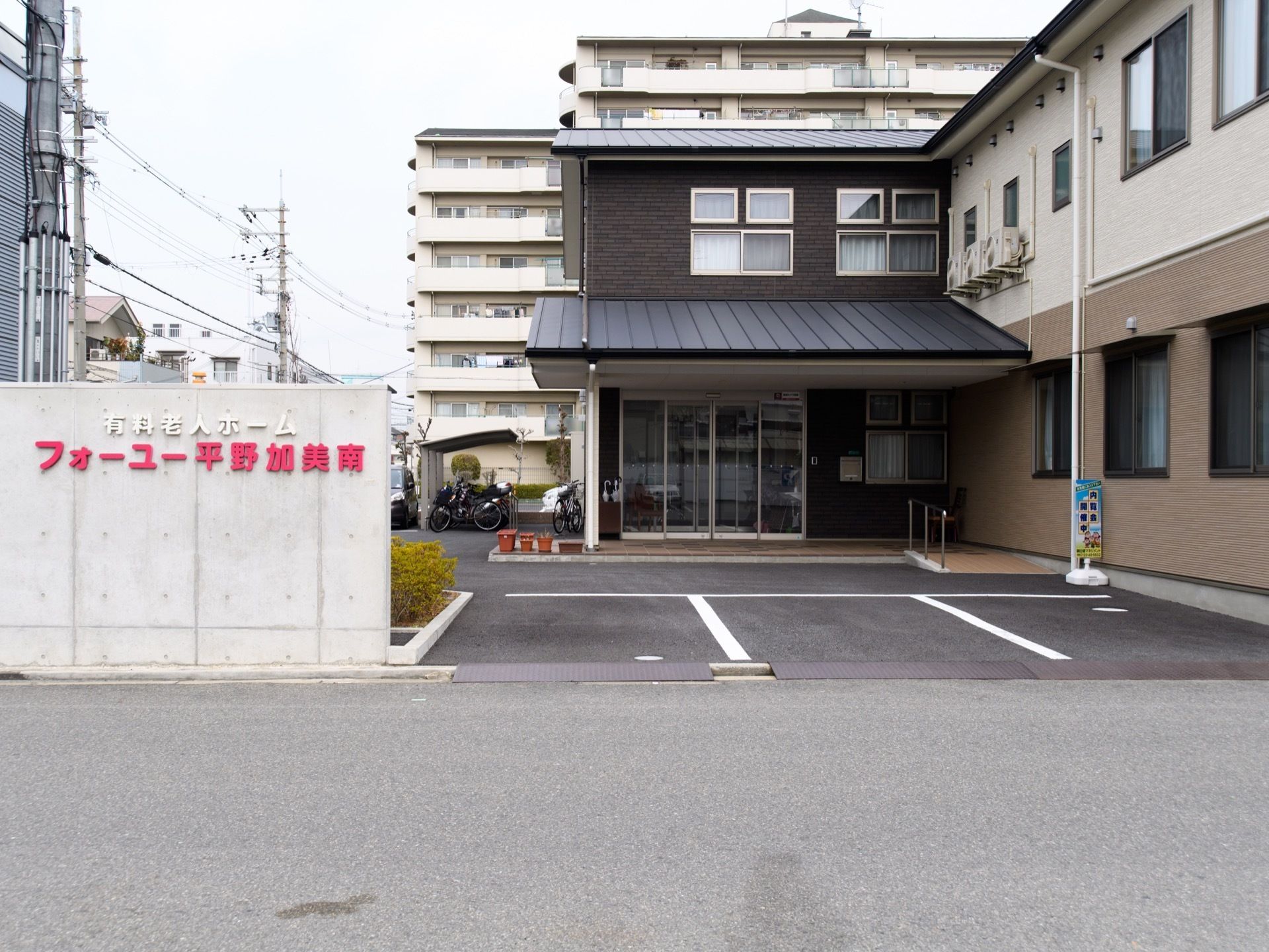 道路に面した塀の壁に、白字で施設種類、その下に赤文字で大きく施設名を掲げている。敷地内には、駐車場、駐輪場を完備している。