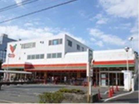 白を基調に朱色とグリーンのラインが入っている建物。建物の左上には、スーパーのロゴと店名が記されている。