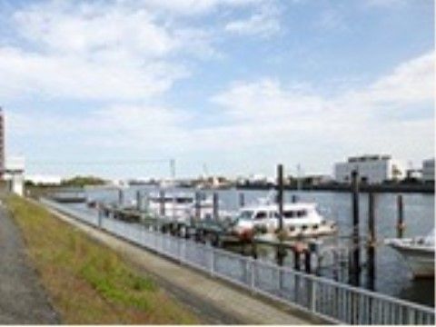 川には船が停泊している。土手の下には川沿いに人が散歩できる程度の通路が続いており、向こう岸にはビルなどの建物が並んでいる。