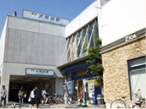 グレーの駅舎の上と入口には、駅名が記されている。入口付近には商店があり、その周辺には自転車が停めてある。