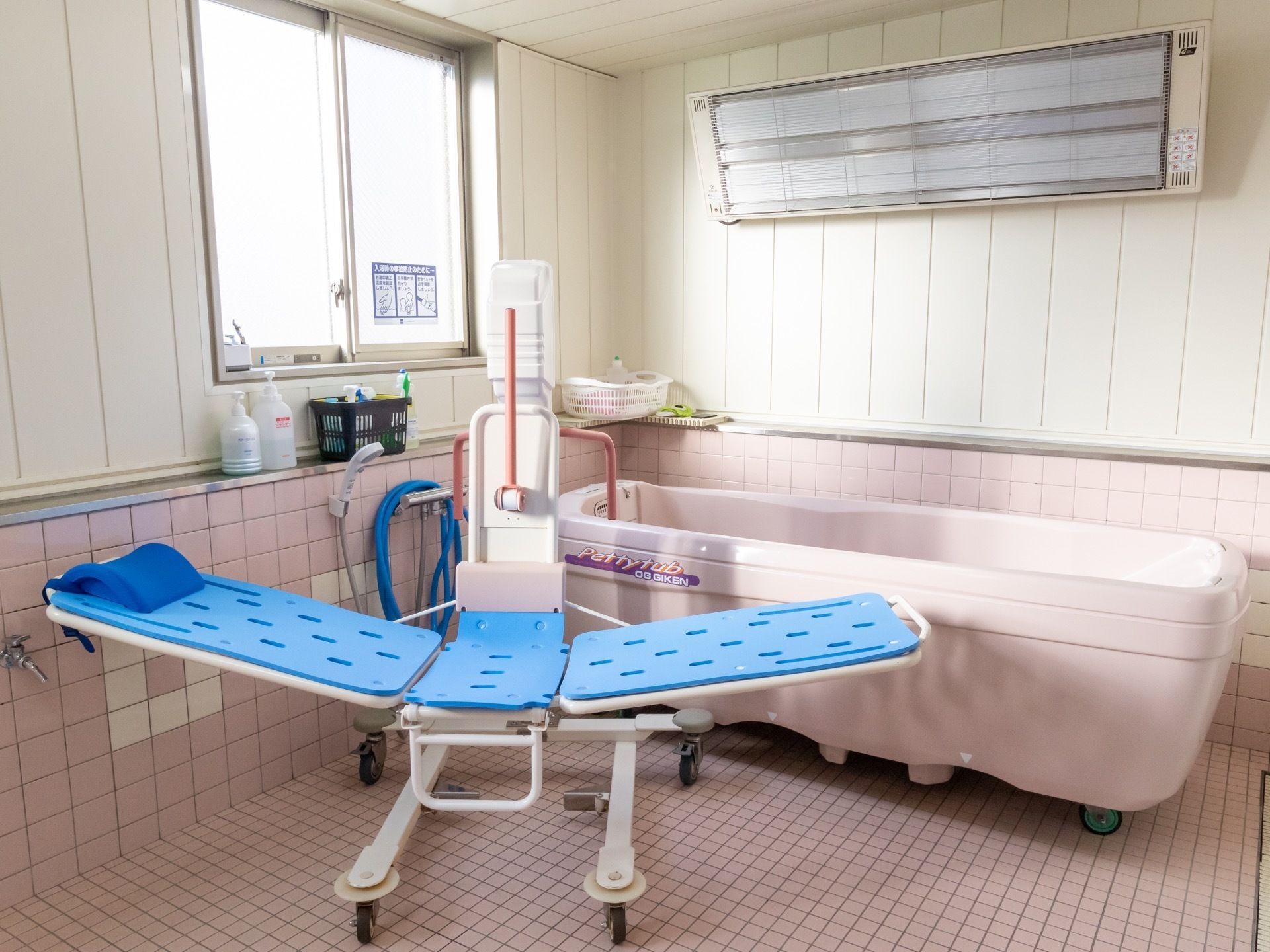 明るく広々とした浴室の奥に、介護浴槽やリフトが置かれている。壁には暖房器具も設置され、入居者様が安全に入浴できる環境が整えられている。