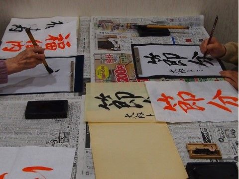 机に新聞を敷いて、節分に関する言葉を習字で書く入居者様