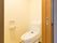 こぢんまりとしたスペースに洋式便器がある。壁にはトイレットペーパーのフォルダーとトイレの操作パネルが取り付けられている。