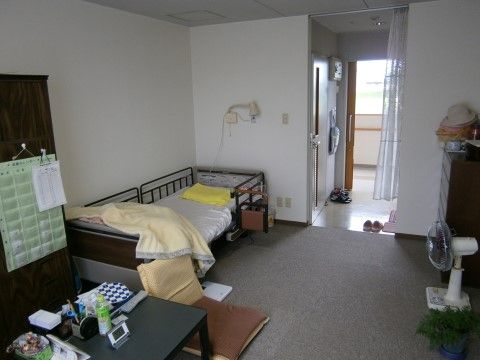 部屋の隅にベッドが置かれ、他にはテーブル、タンス、扇風機がある。窓にはカーペットが敷かれており、玄関の扉は引き戸になっている。