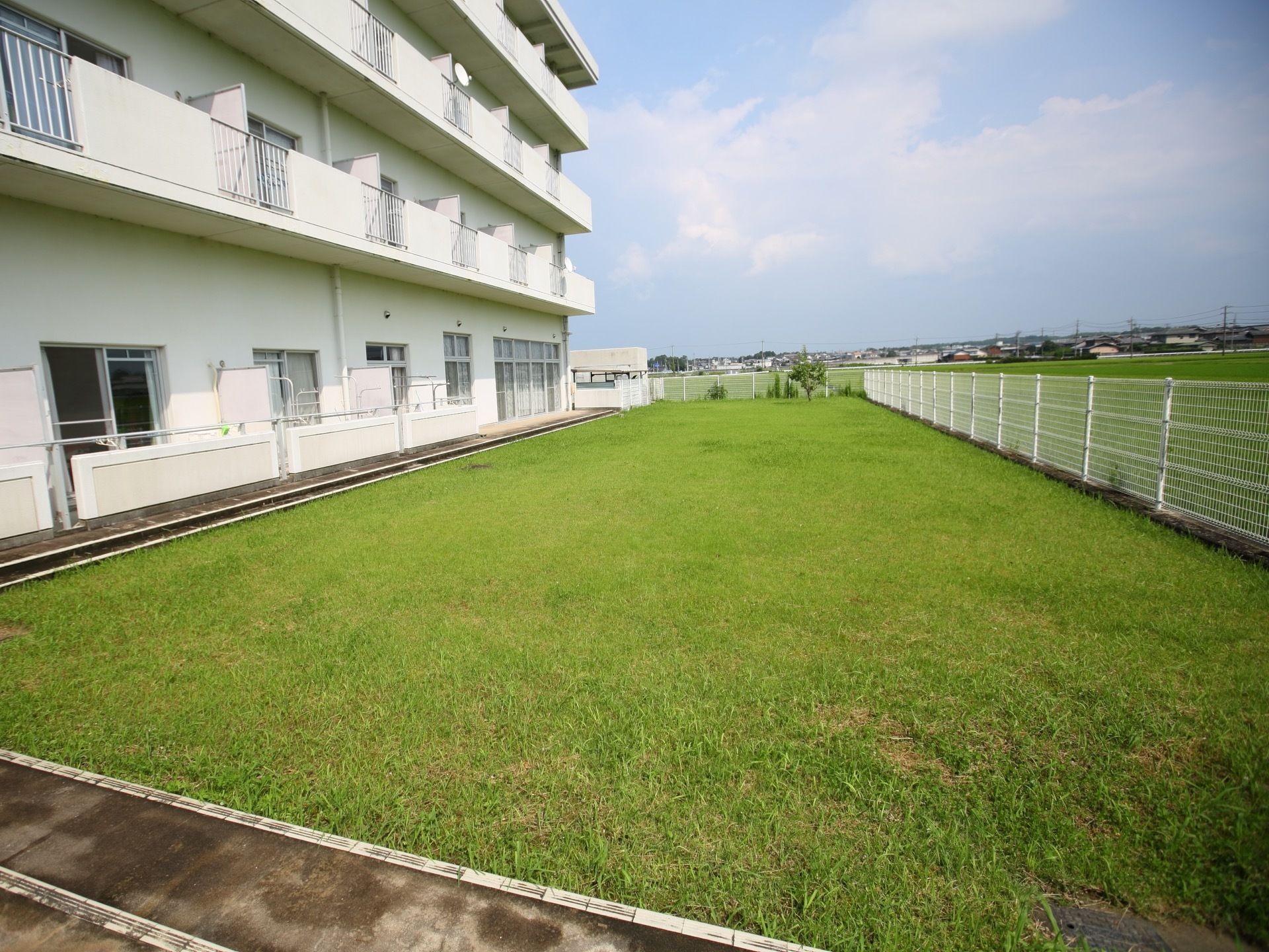 施設は白色の外壁で大きな建物である。周りに建物がなく、芝生などの緑に囲まれた自然あふれる環境である。