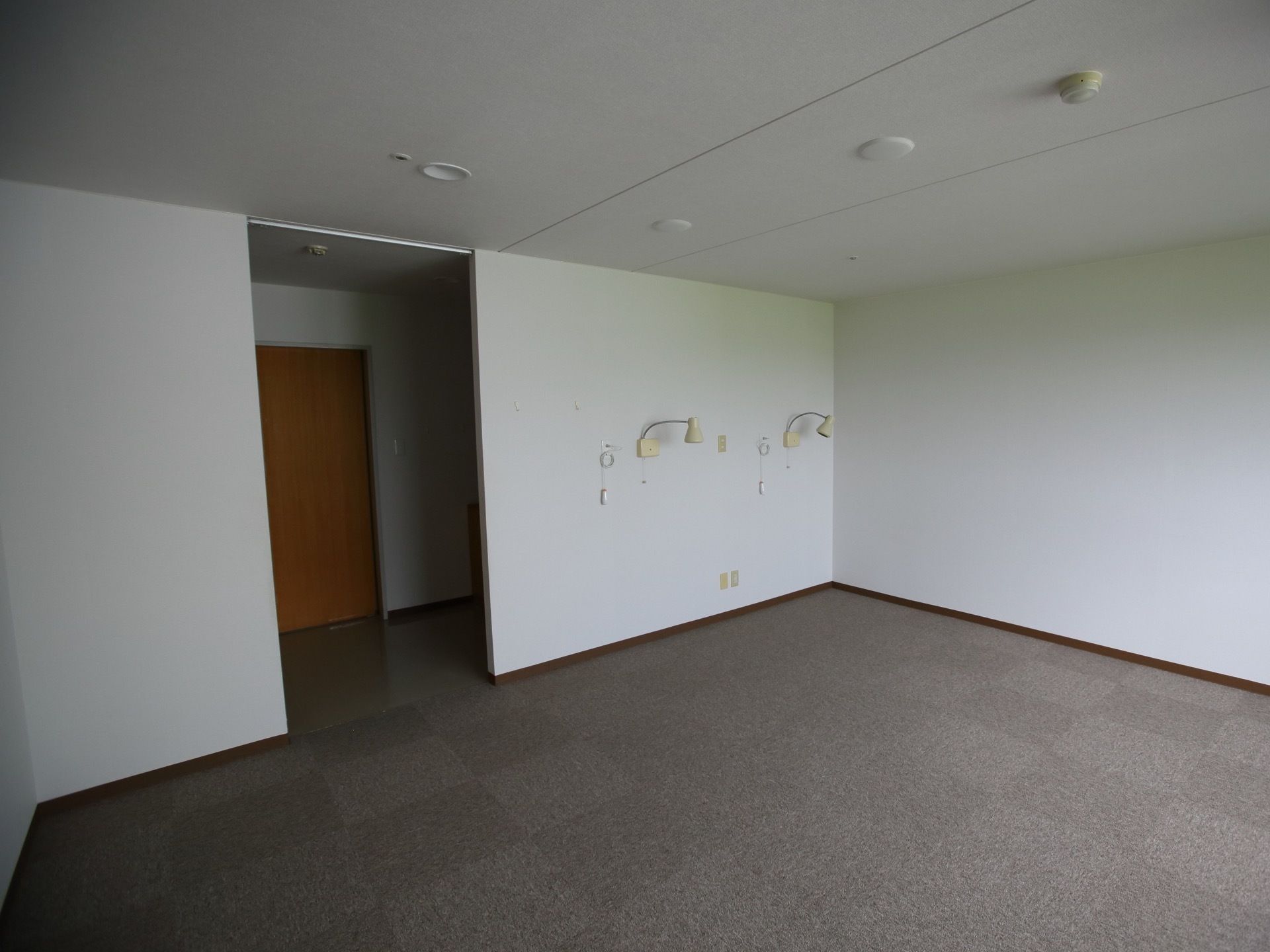 白い壁とグレー色のカーペットが敷かれた落ち着いた雰囲気の居室。広いスペースがあり、２人で入居可能である。