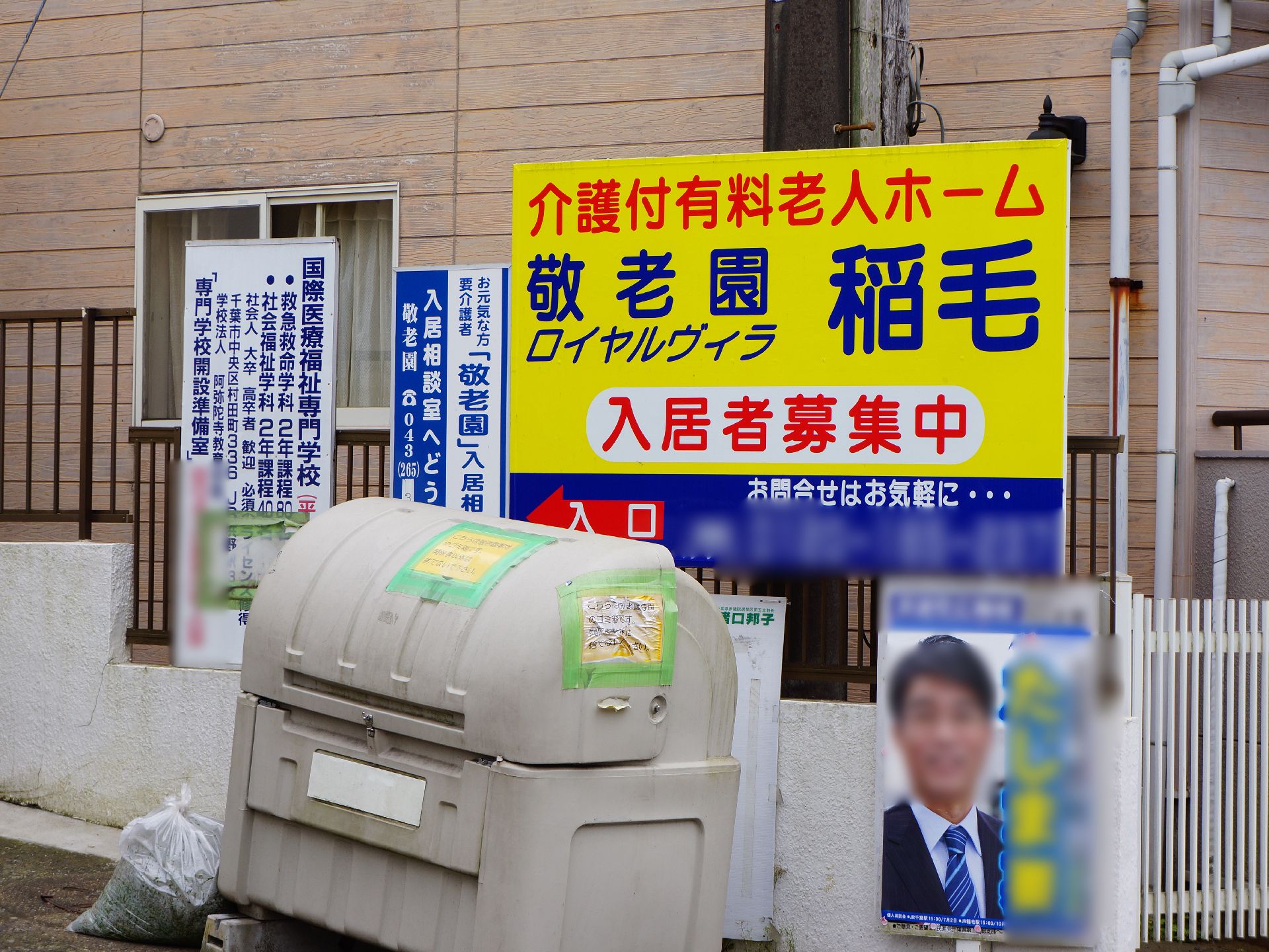 黄色がベースの看板には、青い字で施設名が表示されている。問い合わせも書かれている。その隣には、入所相談室の案内看板も設置されている。