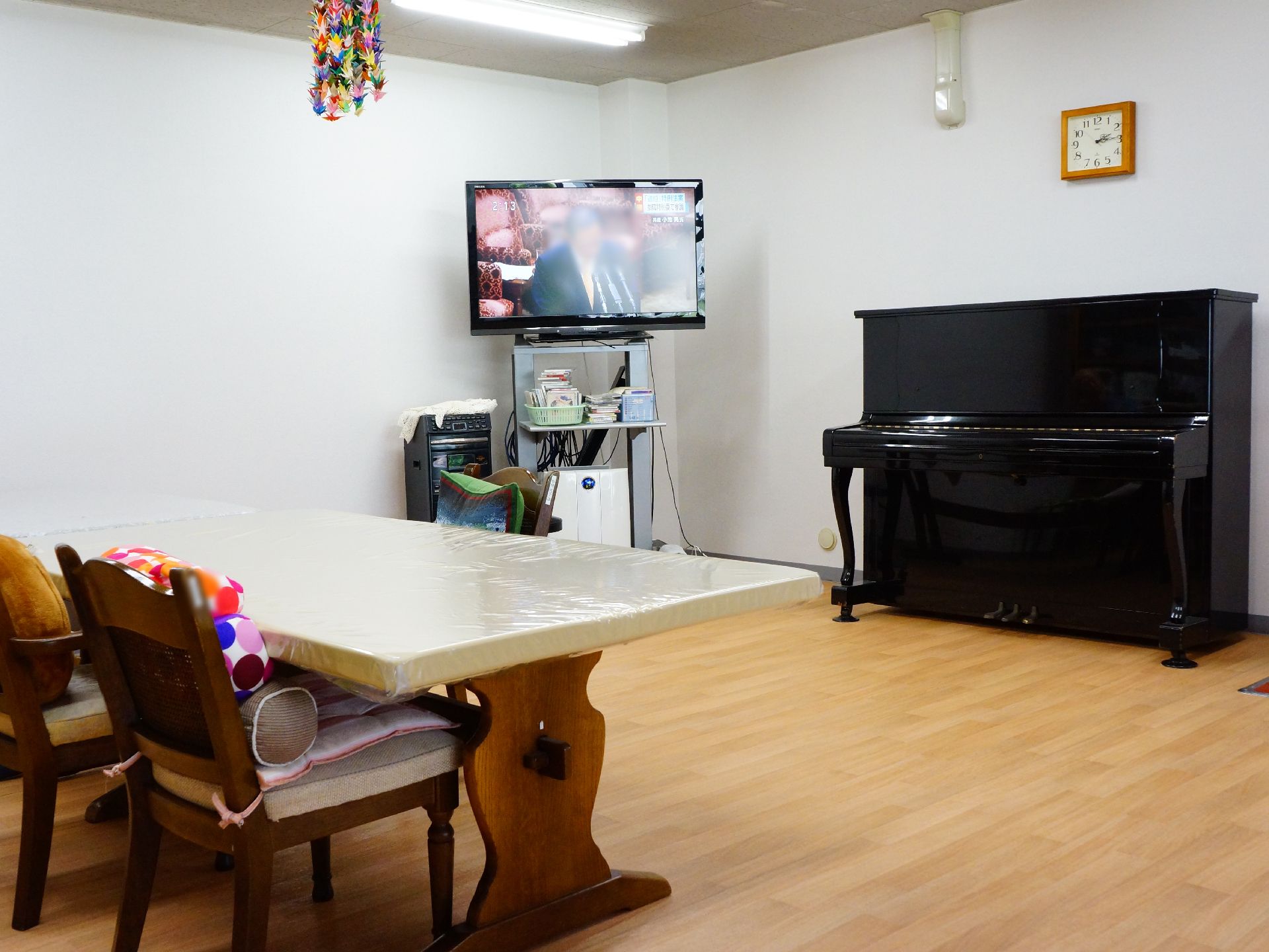 食堂奥にはテレビがある。近くのテーブルは、テレビ側には椅子が置かれていない。カラオケの機械もある。隣にはピアノも置いてある。