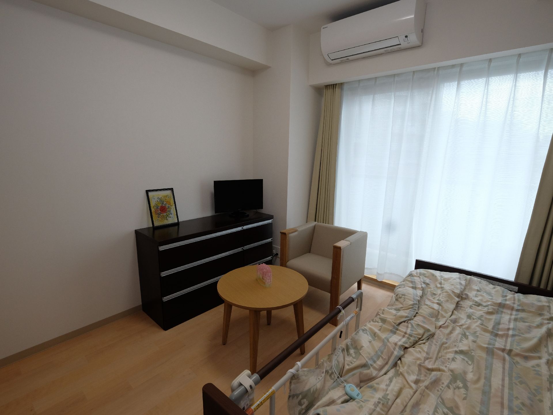 広々としたベランダに面した風通しが良い居室。電動式ベッド、エアコン、チェスト、テレビ等が機能的に置かれている。