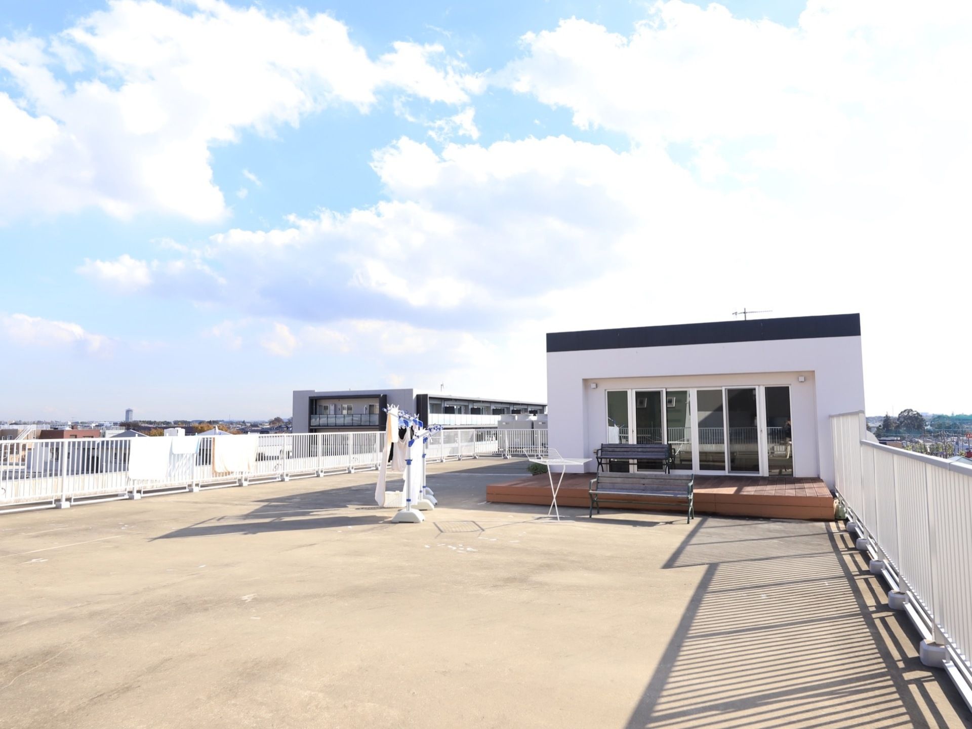 白い柵で囲われた広い屋上がある。掃き出し窓の外にはウッドデッキが設置され、ベンチなどが置かれている。