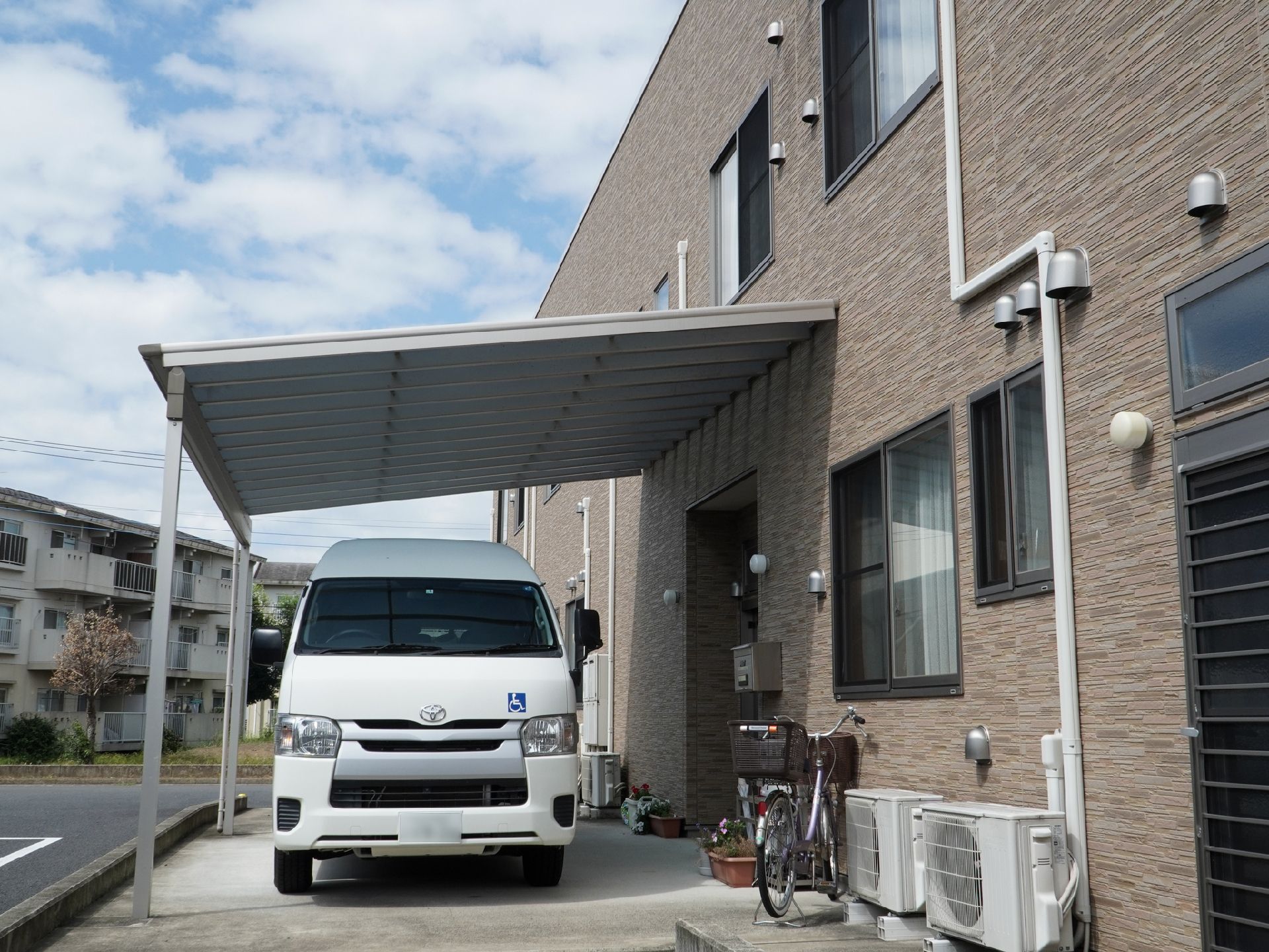 レンガ調の建物の側面についた屋根とその下に止まっている白い車