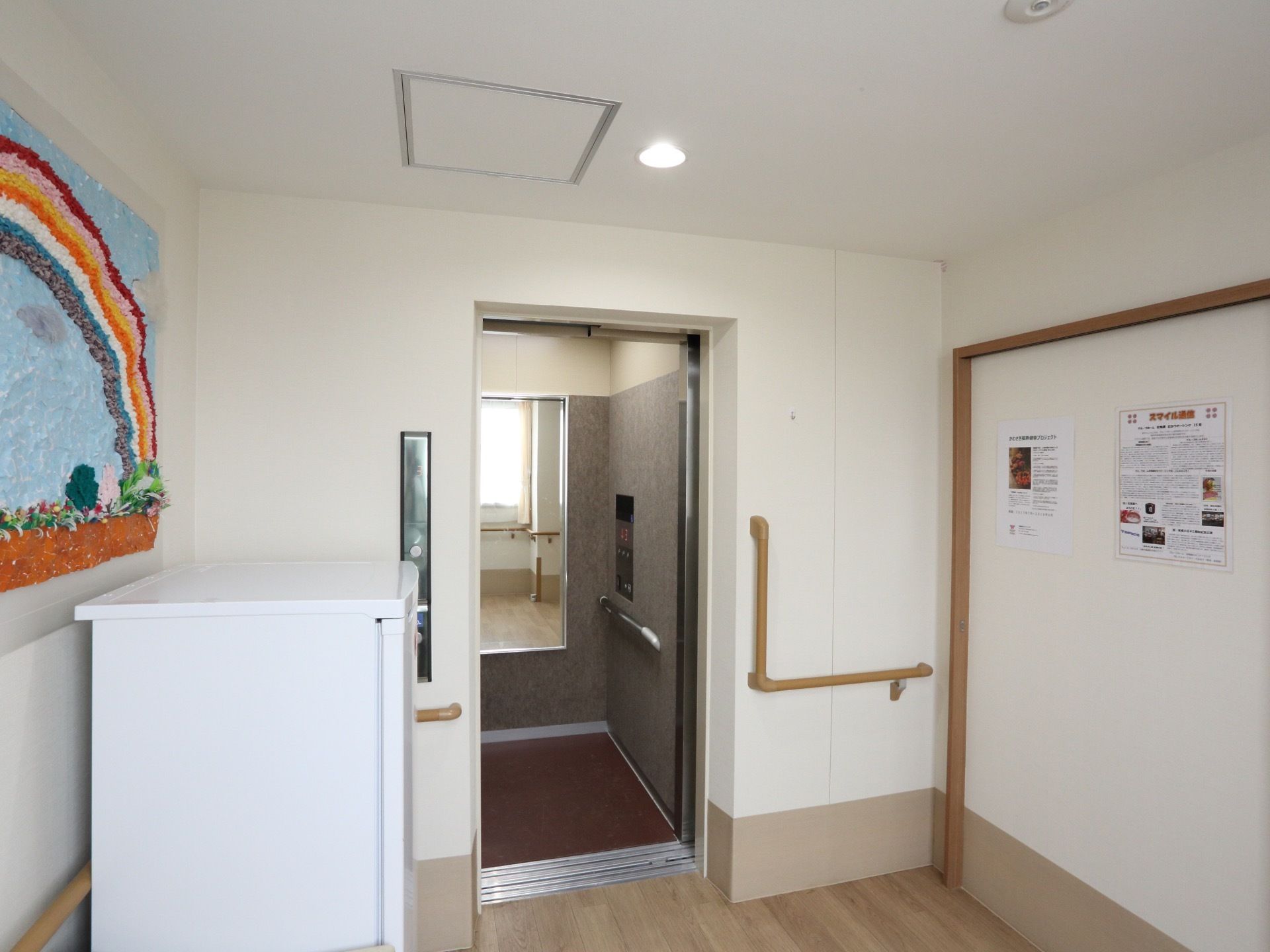 壁には手すりが設置してあり、その上に制作物や行事のポスターが貼られている。奥にはエレベーターがある。