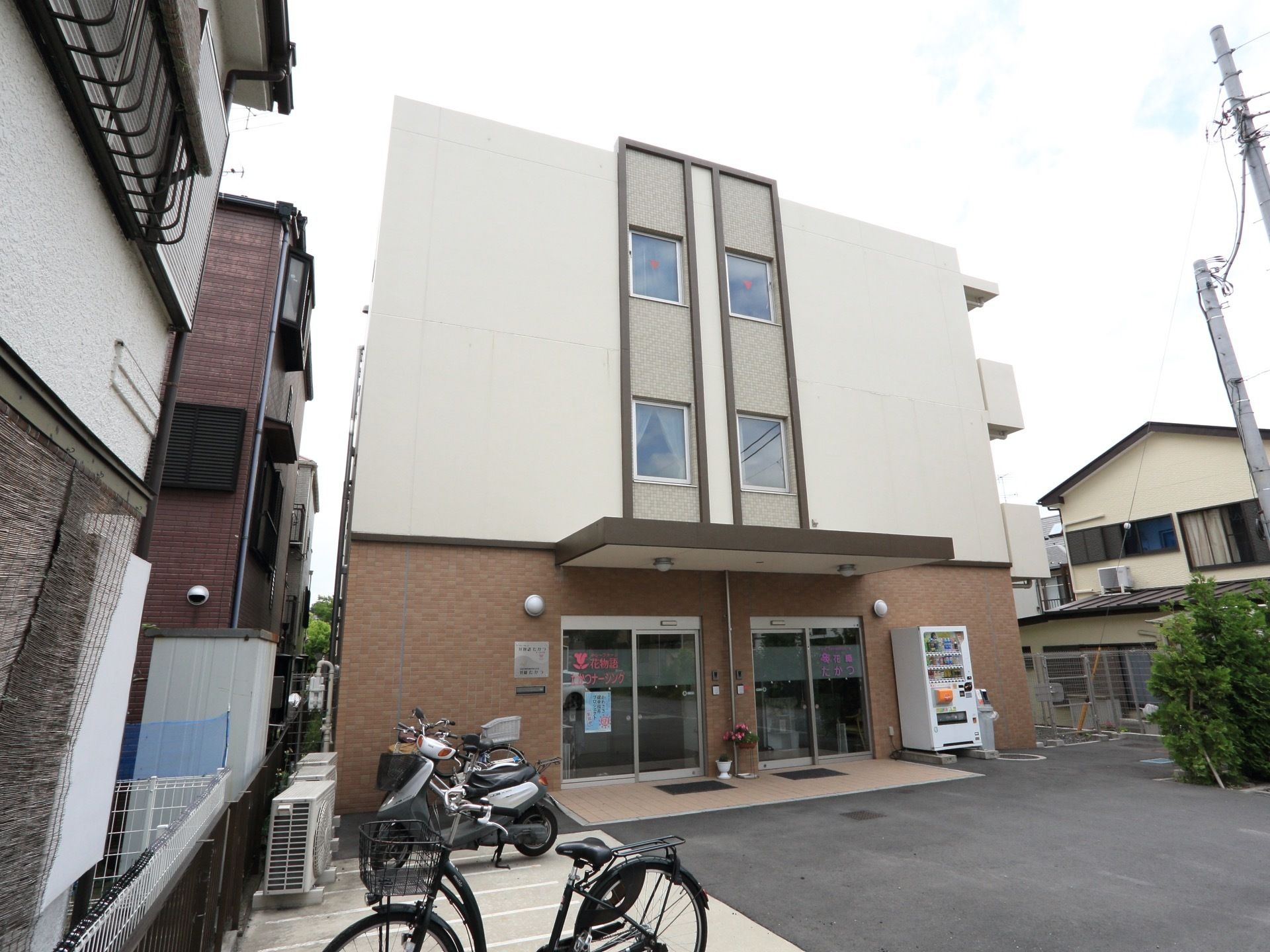 三階建てのグループホーム。駐車スペースがあり、バイクや自転車が停まっている。また、各個室にはバルコニーがある。