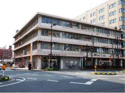 道路沿いの角地に立地している郵便局。外壁はベージュを基調とし、落ち着いた雰囲気になっている。建物前の道路の幅は広くなっている。