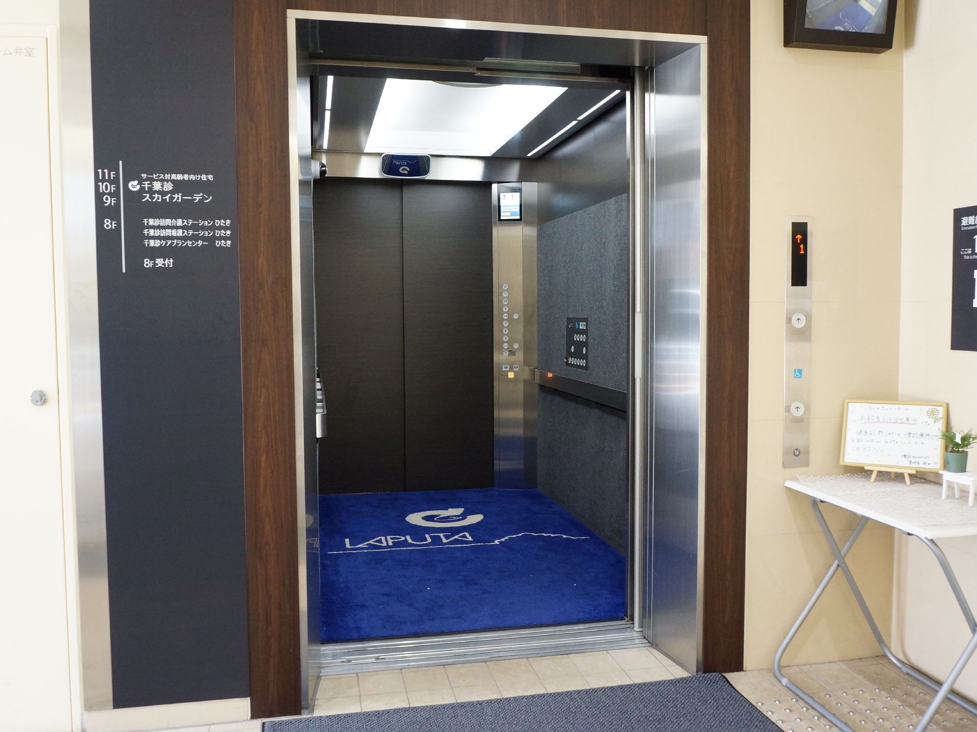 1機のエレベーターがある。エレベーターの扉は出入り口が2つあるものになっているので、乗って体の向きを変える必要がない。