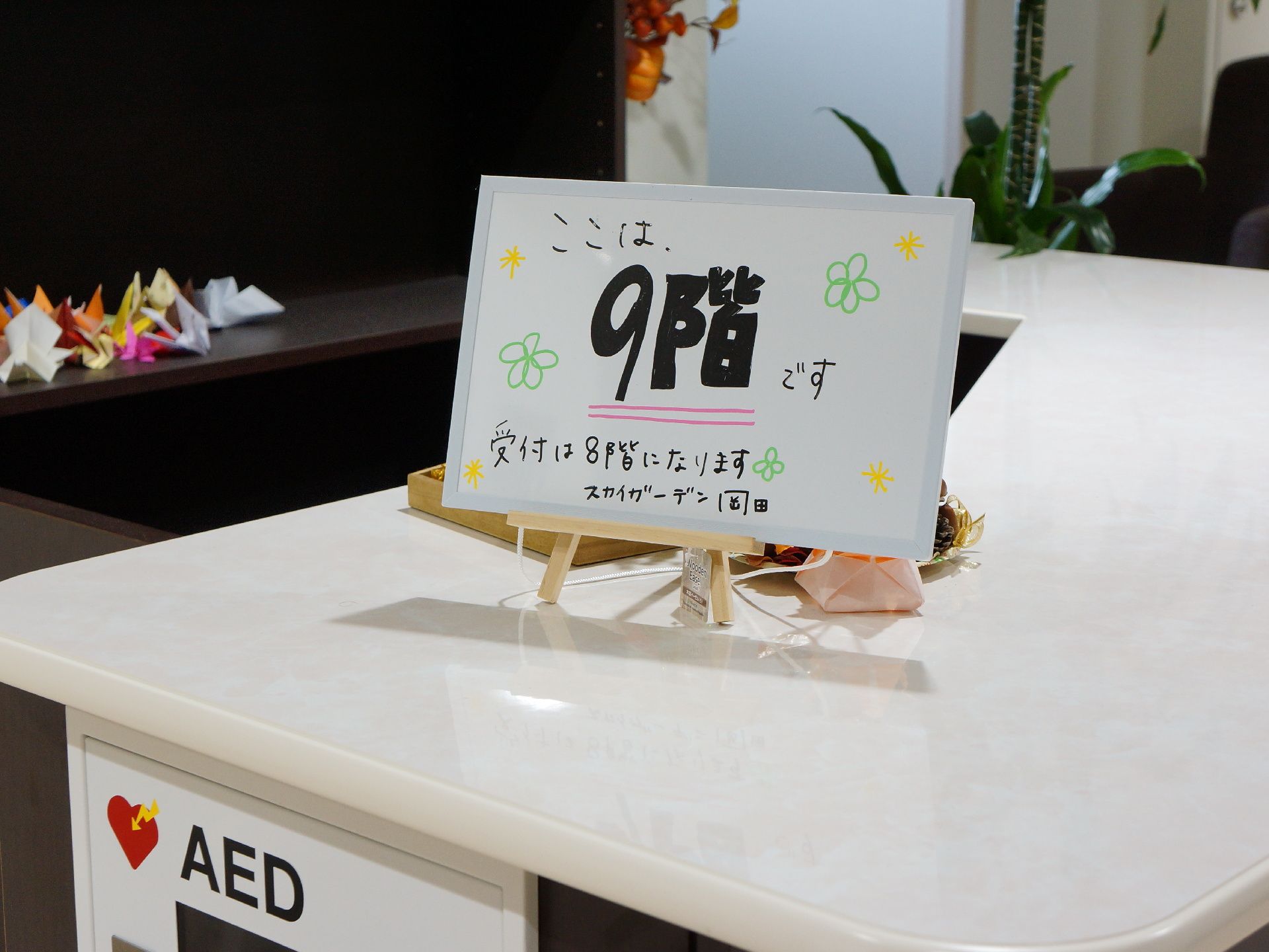 AED装置が設置されたカウンターの上にカードが置かれている。カードにはここは9階であることと受付が8階であることが書かれている。