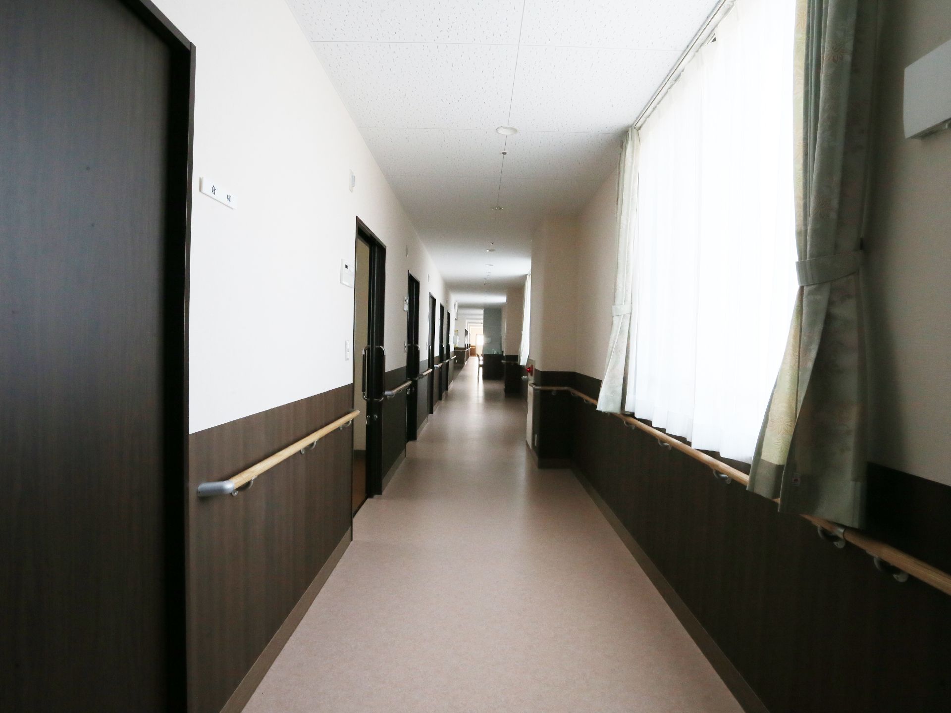 廊下の片側は窓で、もう片側には居室の出入り口がならんでいる。出入り口は黒っぽい木の引き戸である。壁にはずっと手すりが付いている。