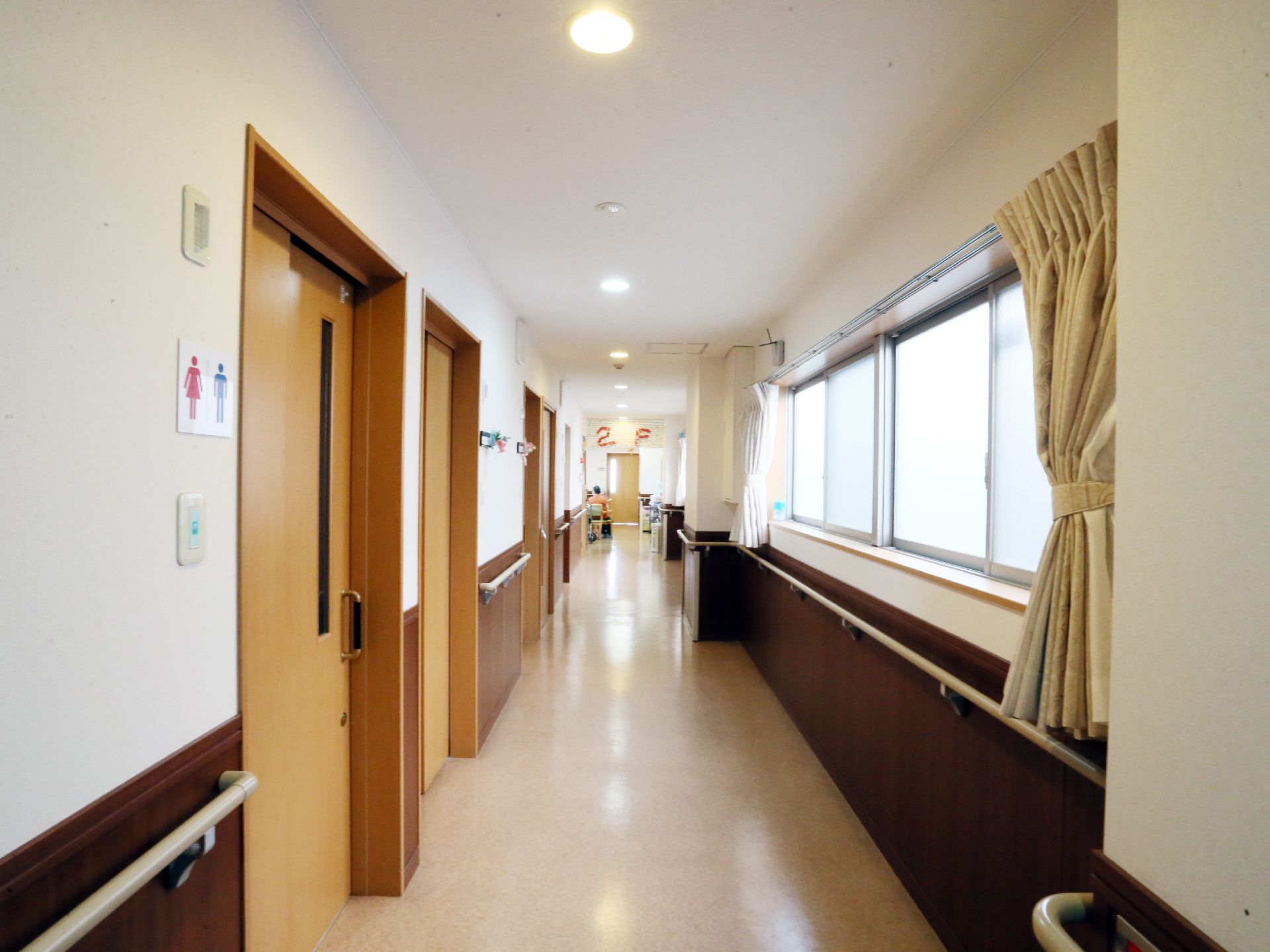 左側にトイレと居室のドアが並び、右側に窓がある明るい廊下