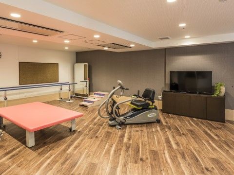 バイク型のトレーニングマシンや歩行練習用の手すり、テレビが置かれた広い部屋