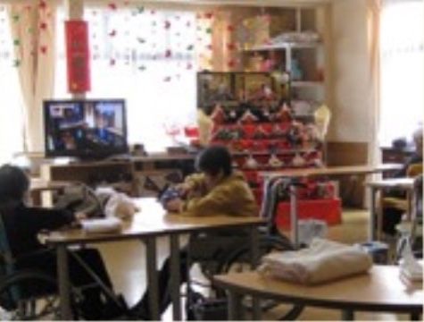 ひな人形が飾られた部屋で、椅子に座ってテレビを見る入居者様