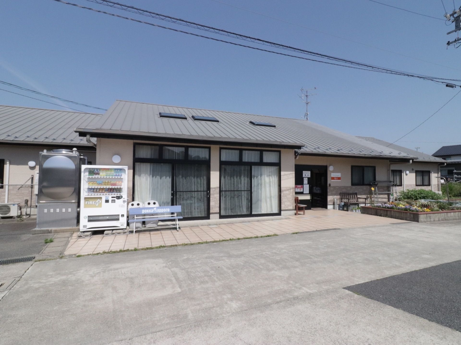 日当たりの良い平屋建てのグループホームである。建物の前には自動販売機や専用のごみ箱、ベンチが置かれている。