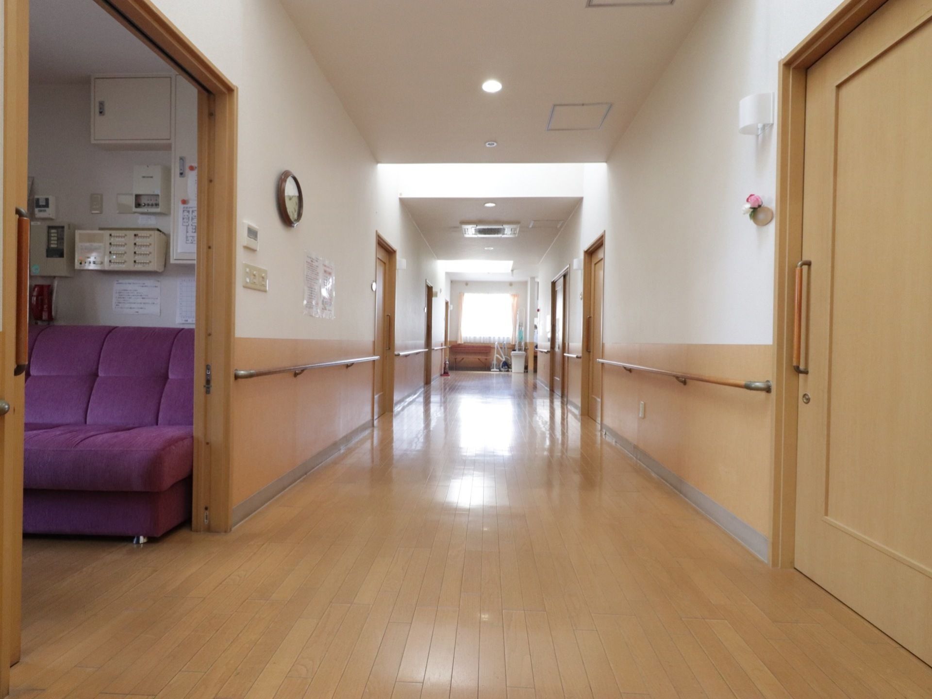あたたかみのあるフローリングの通路で、突き当りに窓がある。両壁に手すりが取り付けられており、時計などが掛けられている。