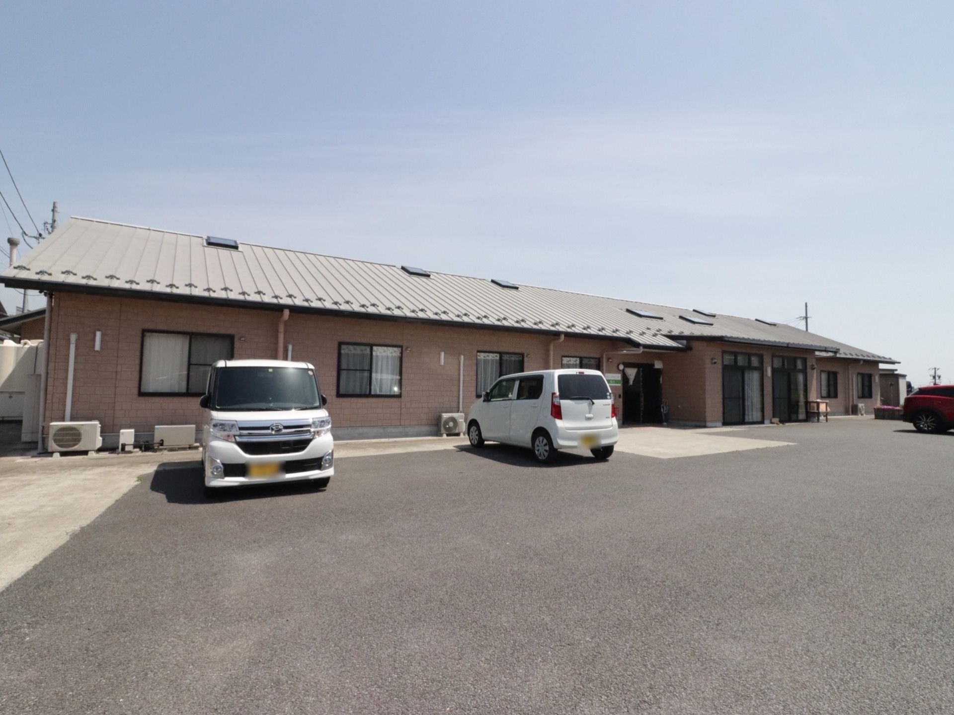 レンガ風の外壁がしっかりした印象の、木造平屋造りの建物。玄関前には、広い駐車スペースが用意されている。