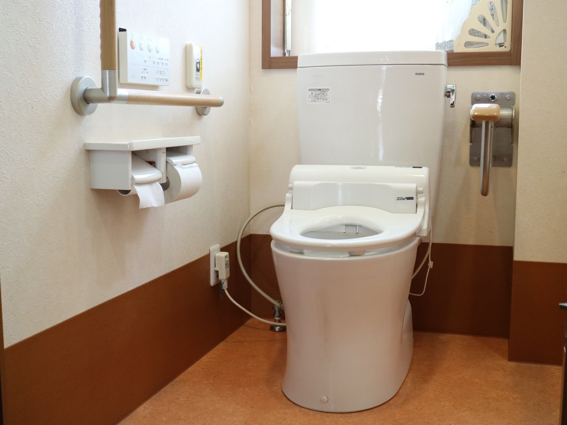 便座の後ろに半透明の窓が付いている。壁に取り付けられた手すりには、掴みやすいように凹凸が設けられている。