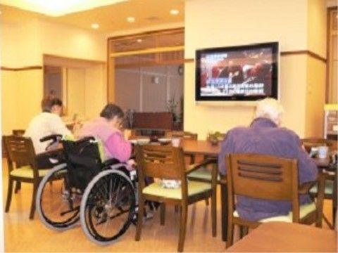 椅子や車椅子に座って、食事をしながらテレビを見る入居者様たち