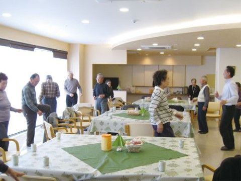 大きなテーブルが並べられた部屋で、体操をする入居者様たち